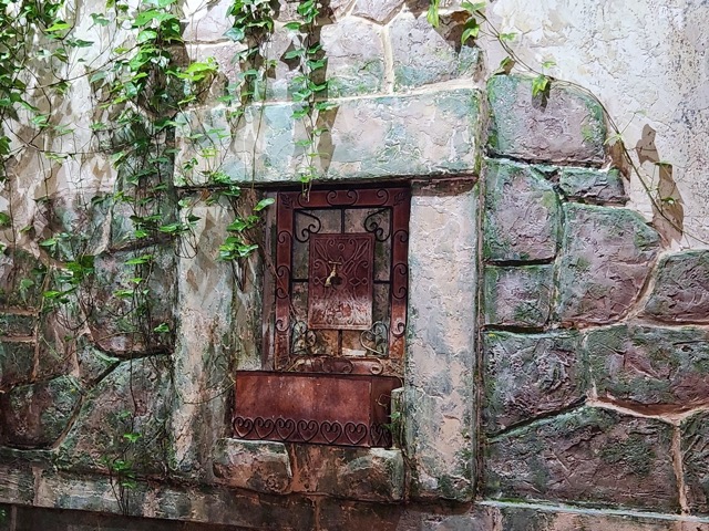 tiny antique faucet peeps out against a brick wall, ivy dangles above it 